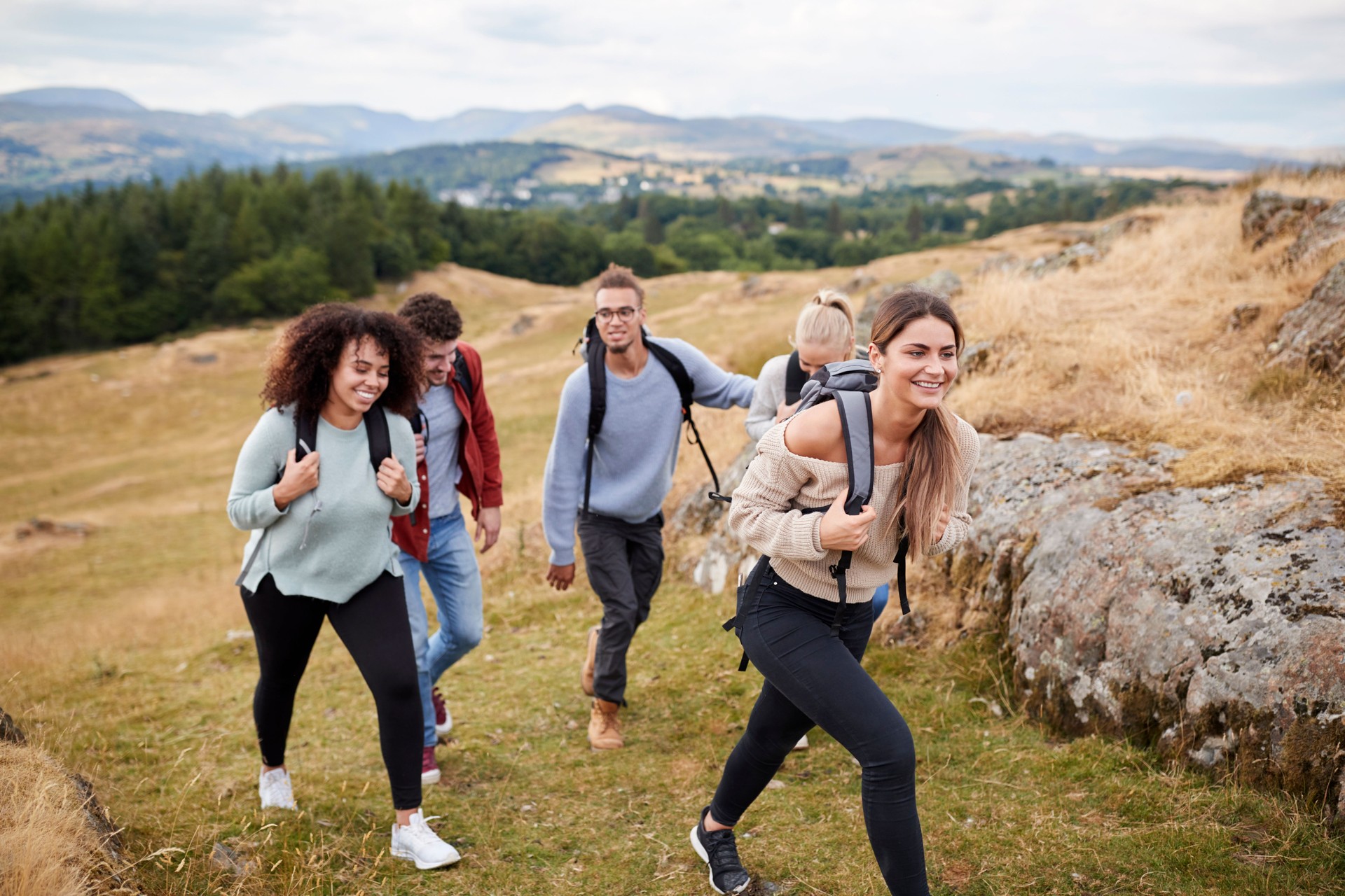 Multi ethnic group of five young adult friends hiking across a field uphill towards the summit, close up